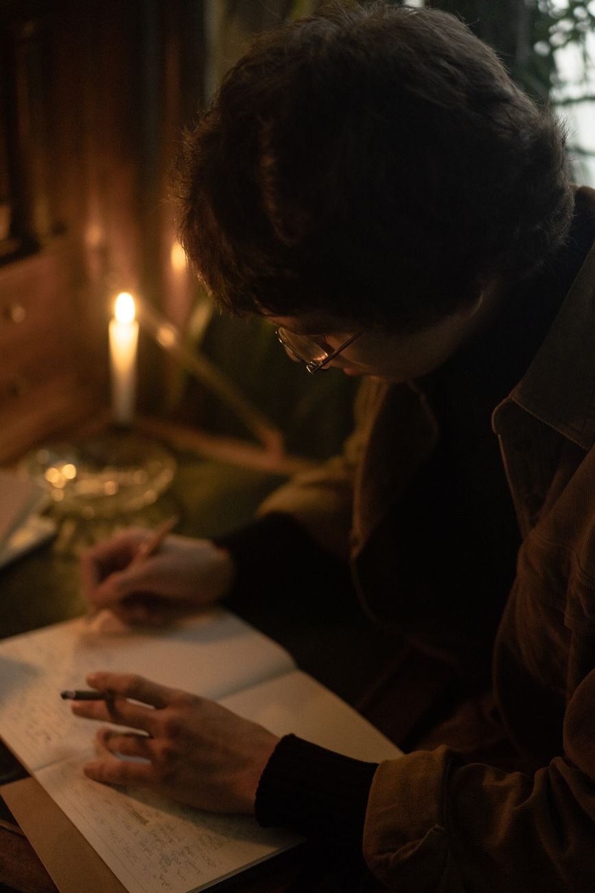 Adult writing in a notebook by candlelight, creating a warm and moody ambiance.